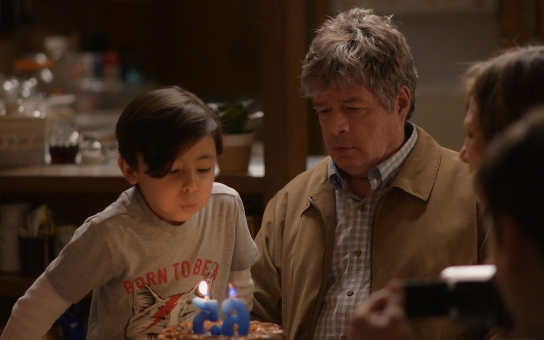 Fotograma de Amores incompletos: un niño sostiene un pastel con velas junto a un hombre mayor en una reunión familiar