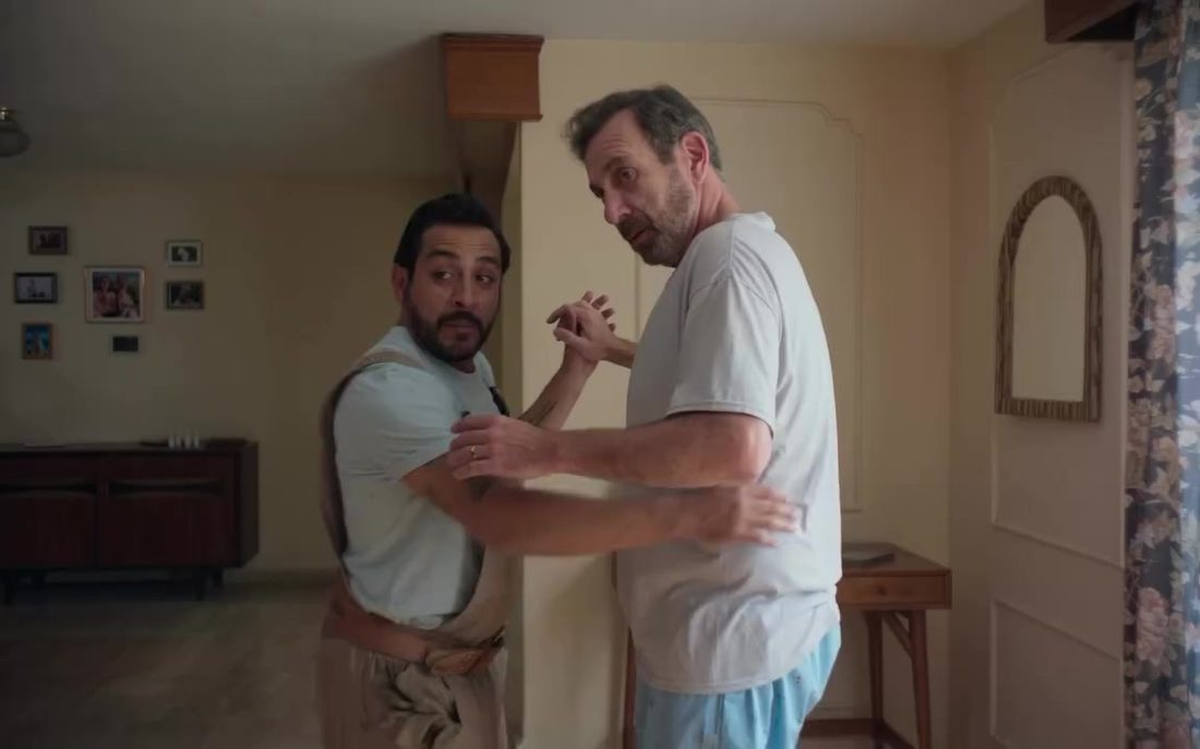 Fotograma de Bailando solo: dos hombres ensayan pasos de baile tomados de las manos en una sala