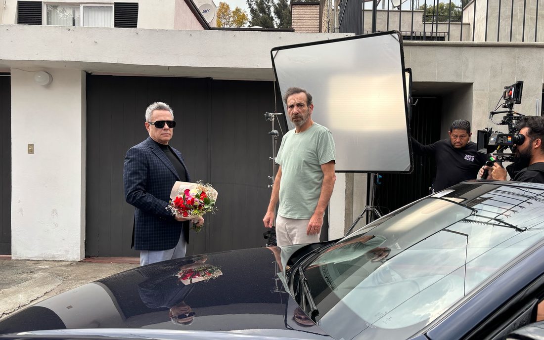 Rodaje de Bailando solo en exteriores: un actor con flores junto a un auto, un difusor de luz y el equipo de cámara