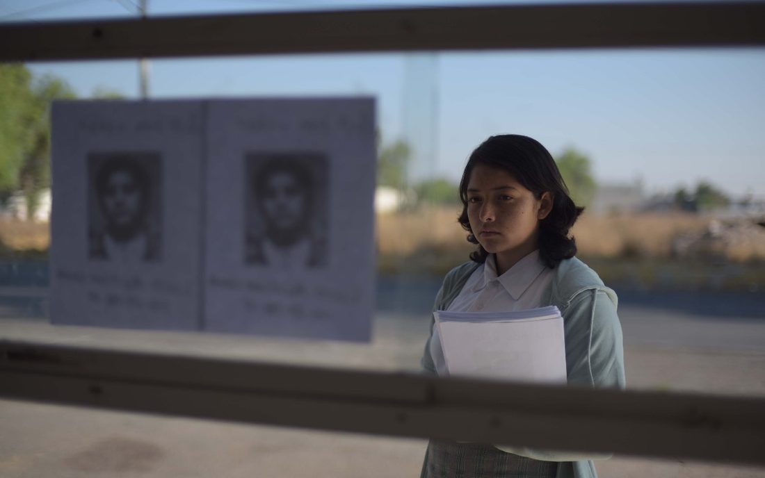 Fotograma de Vergüenza: una joven mira carteles de personas desaparecidas pegados en una ventana